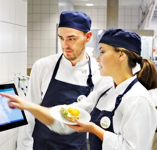Two IKEA co-workers walk down the self-service aisle of an IKEA store. One is pushing a trolley.
