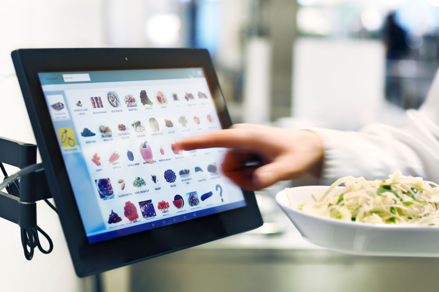 A person's hand pressing icons on a computer touch screen, with a plate of food nearby.