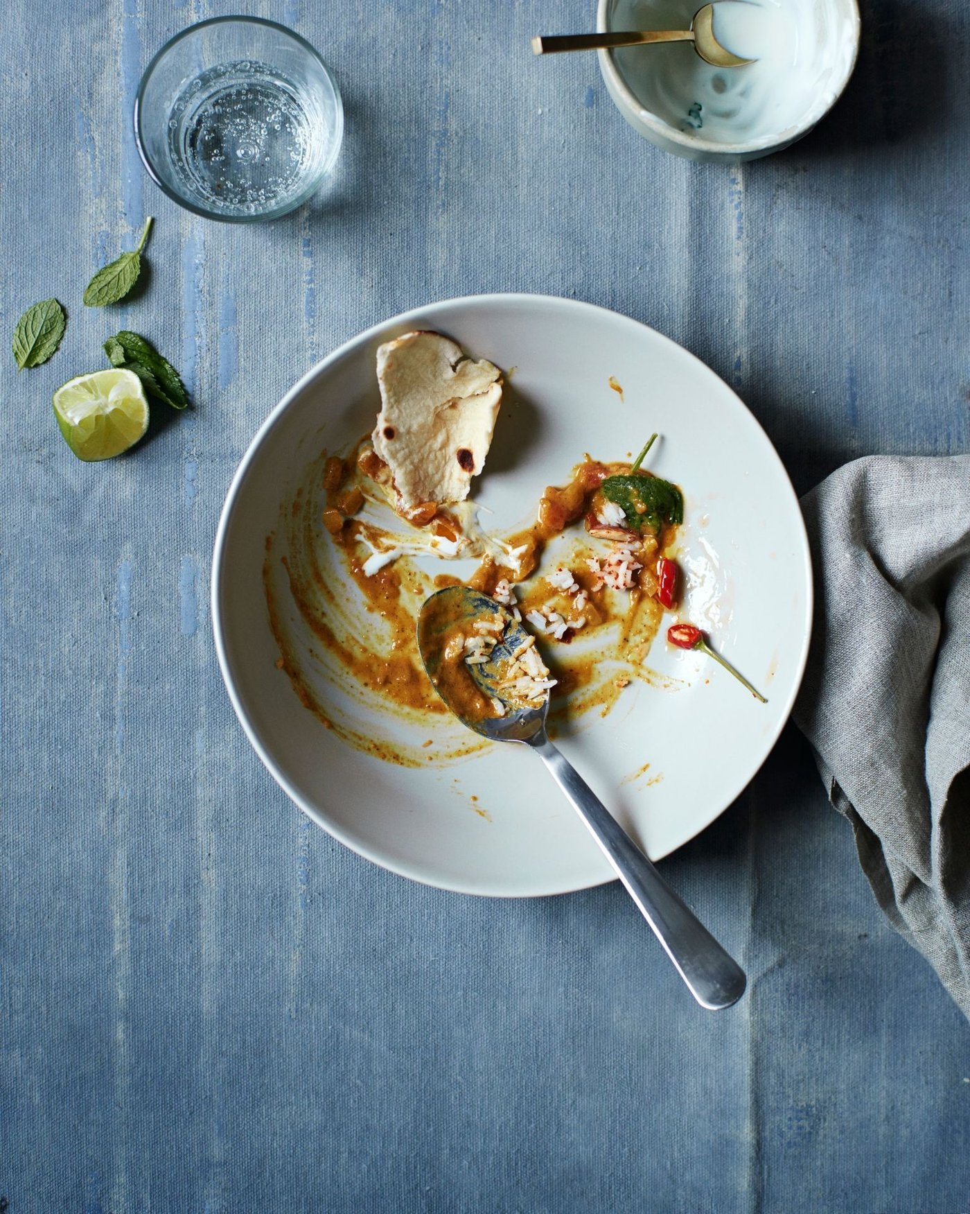 A bowl with food and a spoon on a grey tablecloth covered surface.
