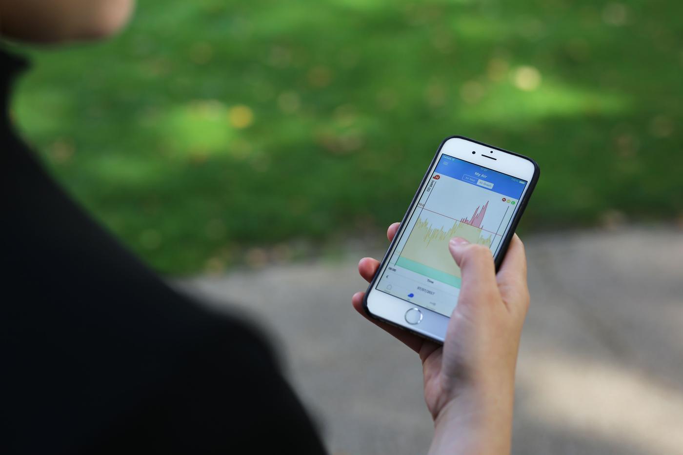 A hand holds a mobile phone outside.