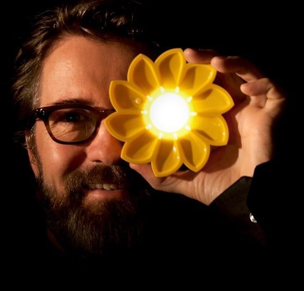 A person holds an illuminated, flower-shaped portable lamp in front of their one eye.