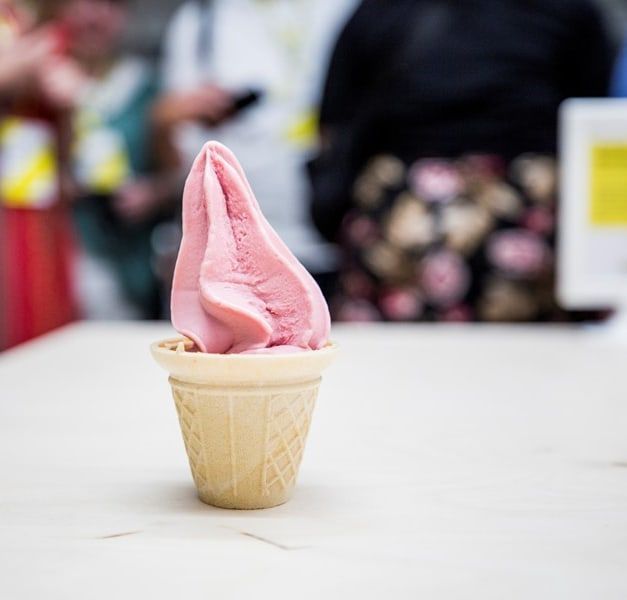 A cup of strawberry soft-serve ice cream on a white surface.