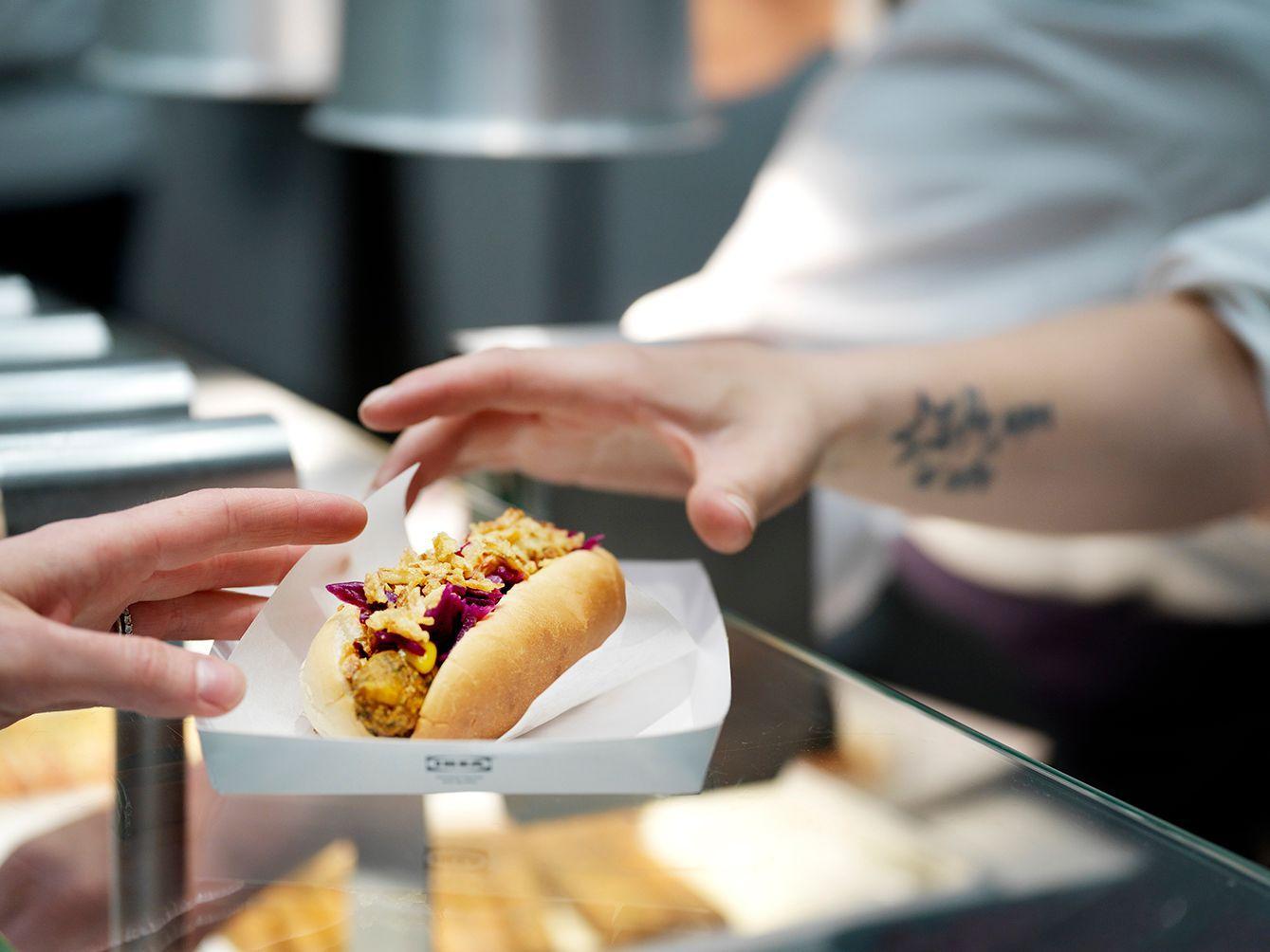 A hand grabs an IKEA veggie hot dog at an IKEA Bistro counter.