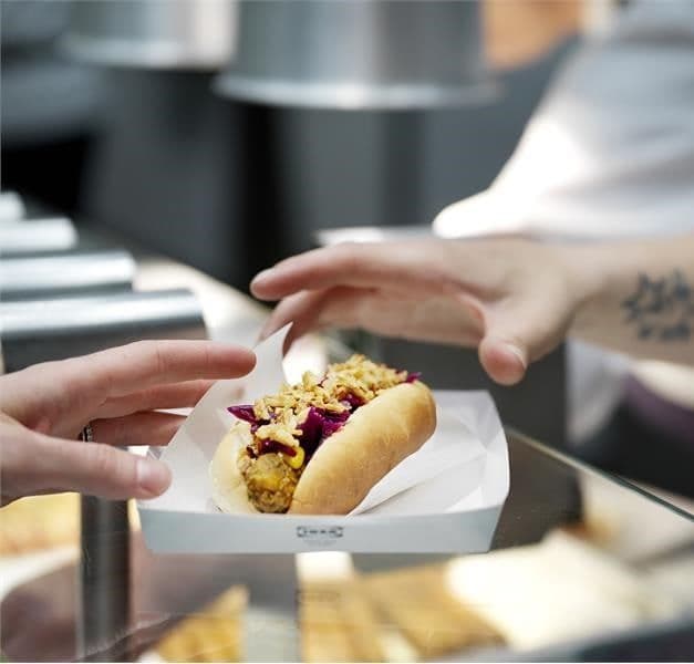 A hand grabs an IKEA veggie hot dog at an IKEA Bistro counter.