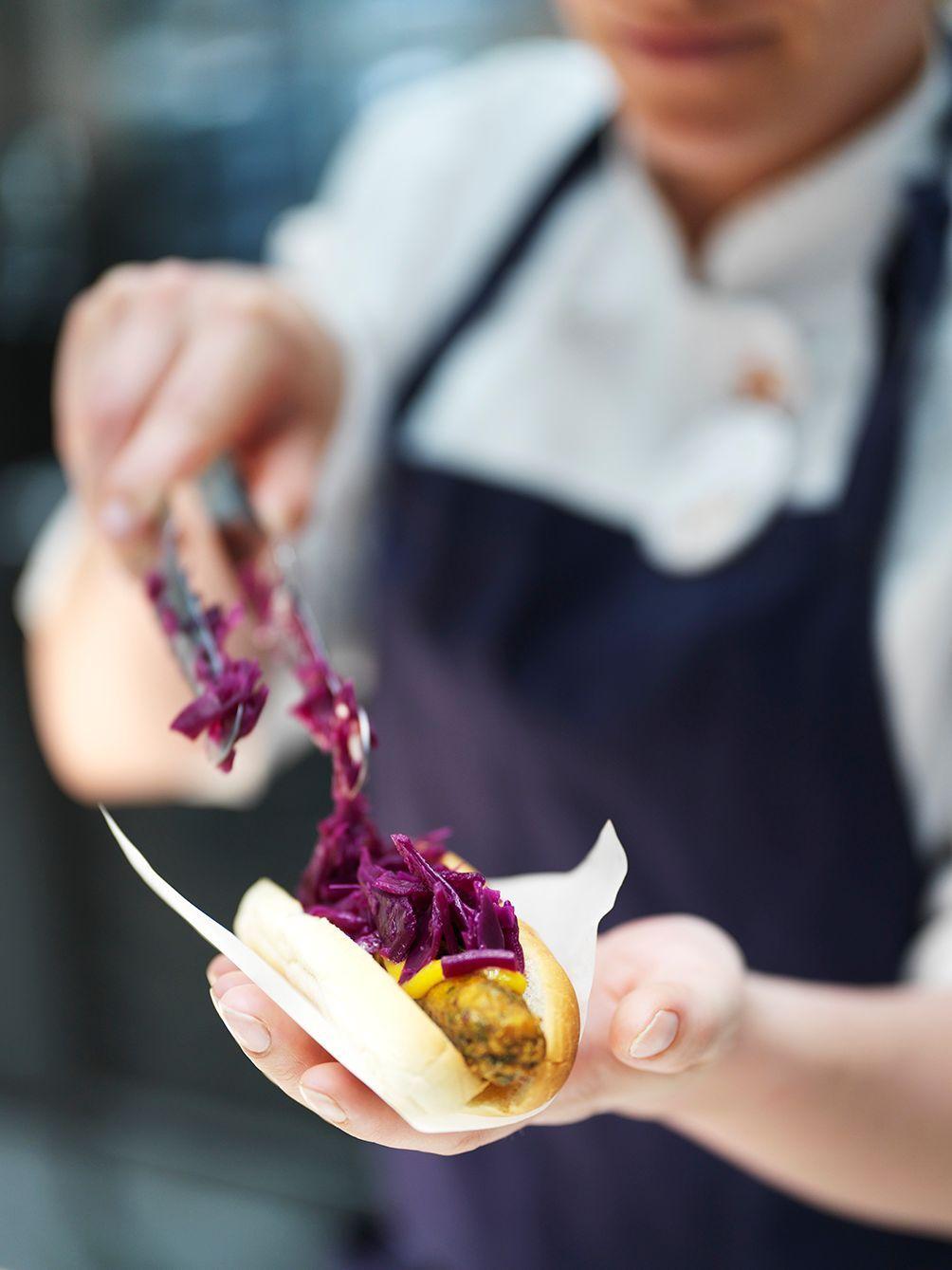 An IKEA bistro co-worker adds toppings to a veggie hotdog.
