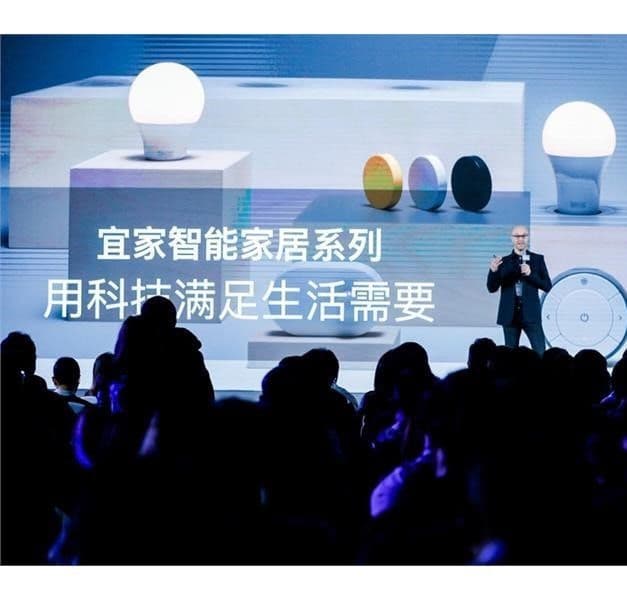 A person on a stage in front of a large audience, with IKEA smart light bulbs being presented on the screen behind.