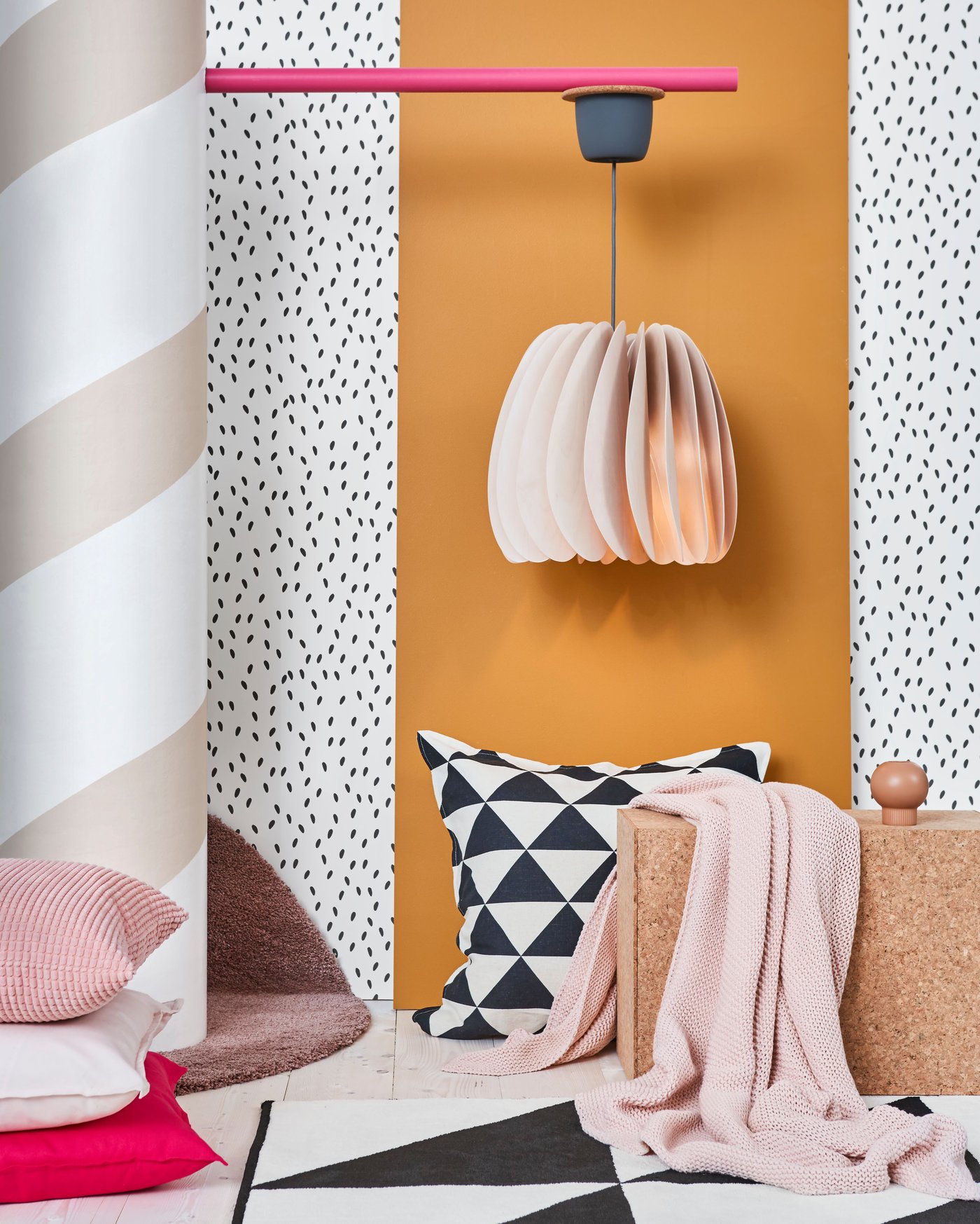 Playful studio setting with bright patterned walls, graphic cushions and SKYMNINGEN pendant lamp.