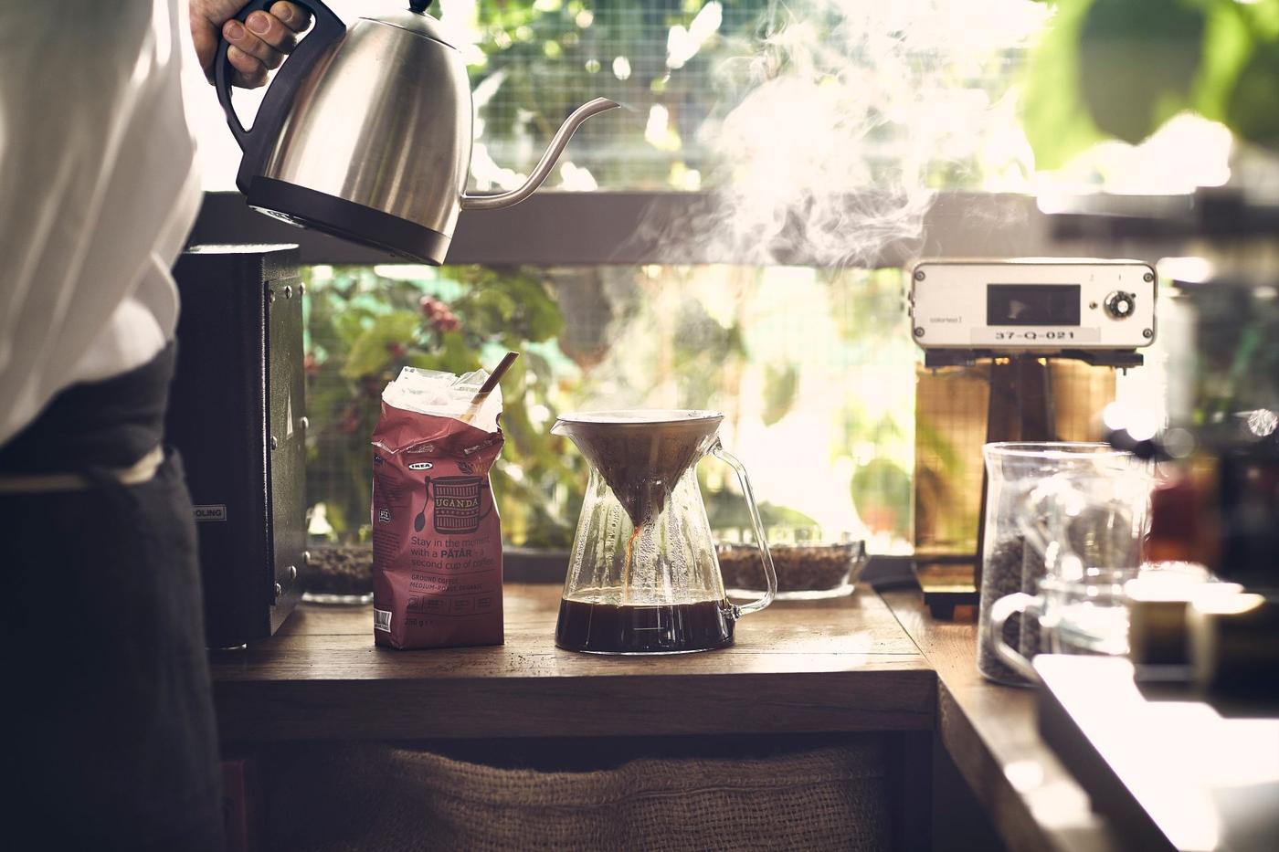 A person pours hot water over coffee grounds on a worktop in the corner of a kitchen.