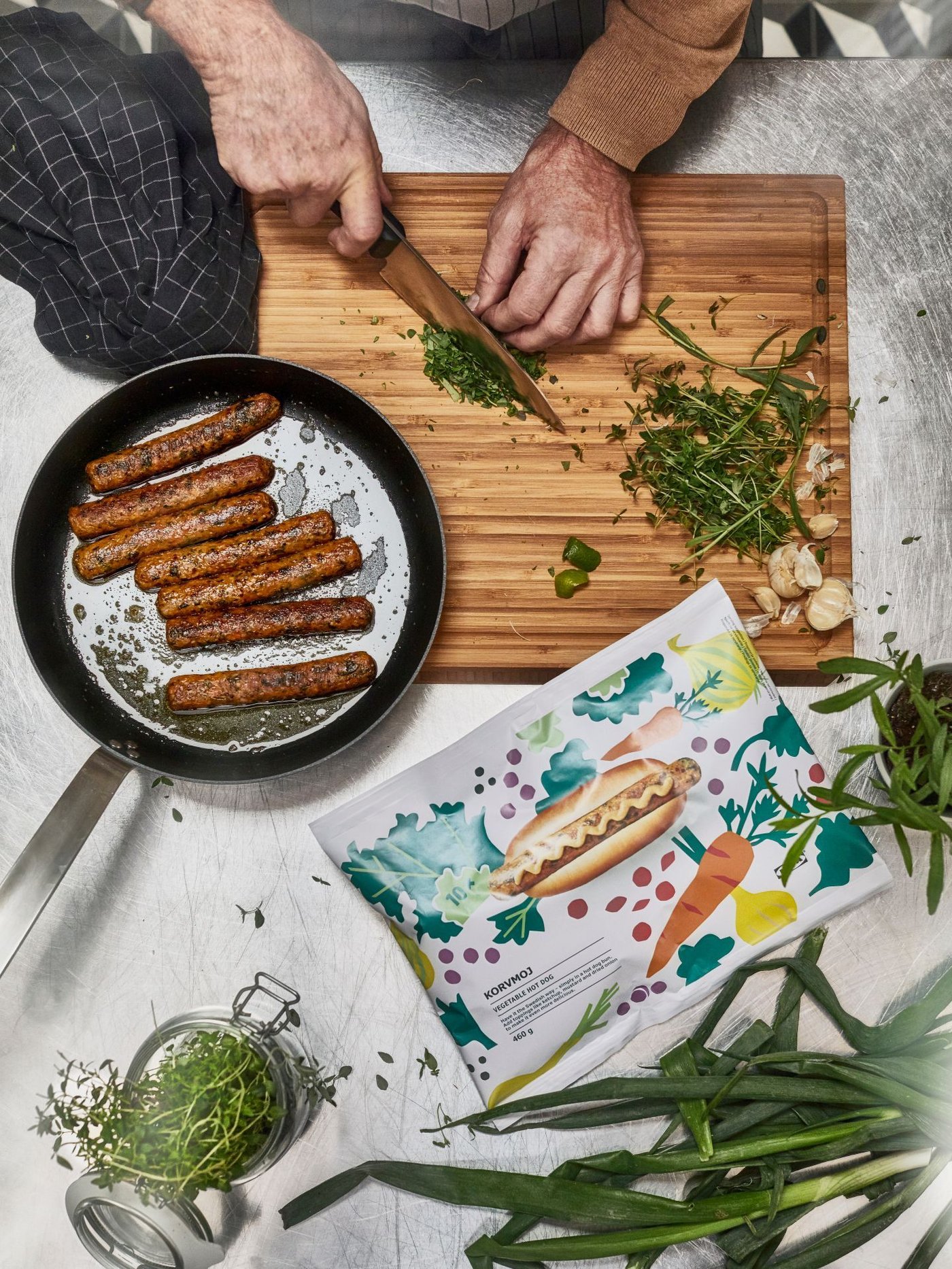 Overvhead view of a person chopping herbs on a wooden cutting board with a package of KORVMOJ veggie hot dogs nearby.