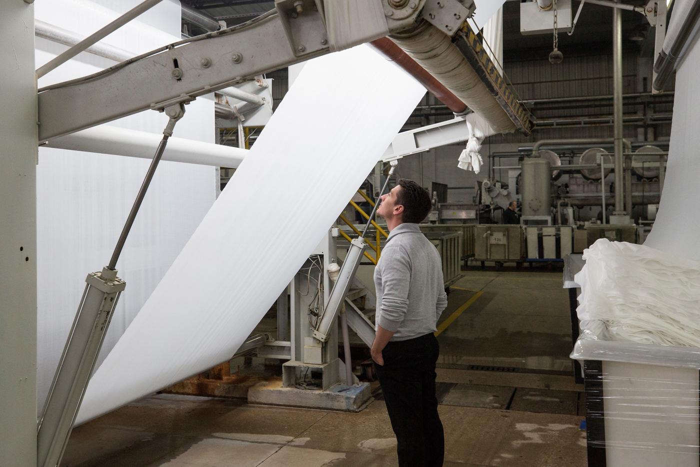 A man inspects fabric on a roll. The fabric is illuminated from the back. 