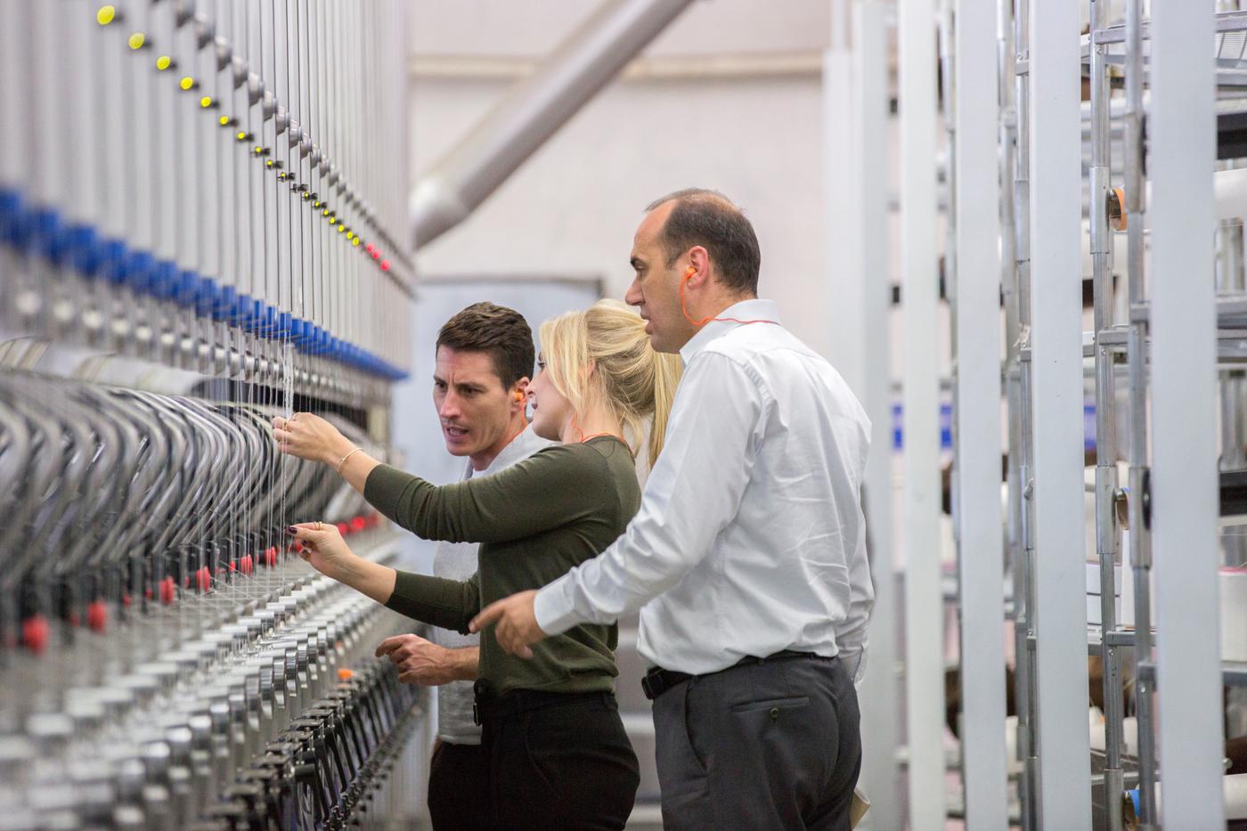 Three people inspect different threads in a factory.