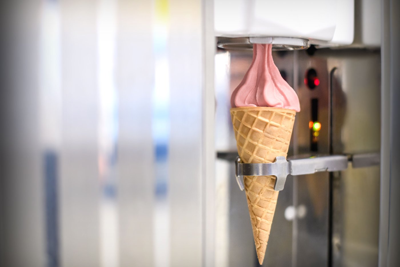 An ice cream machine adding strawberry soft serve to an ice cream cone.