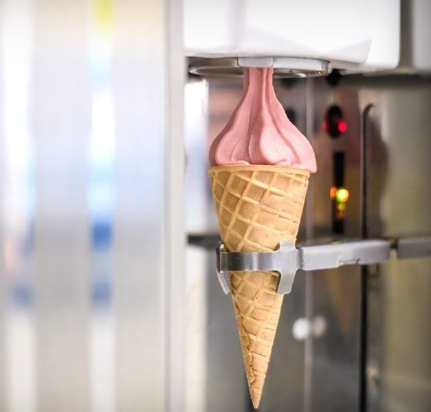 Machine dispensing pink soft serve into an ice-cream cone.