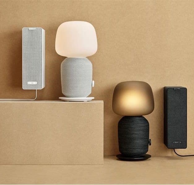 Two speaker lamps and two bookshelf speakers from the SYMFONISK series displayed on a warm sandy-coloured background.