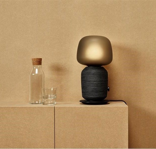 SYMFONISK WiFi speaker lamp displayed on top of a cabinet next to a water carafe and glass in a warm sand-coloured roomset.
