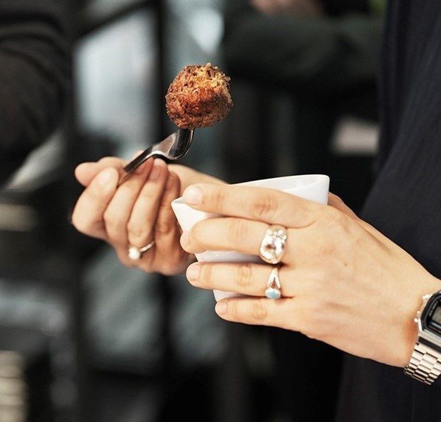 A hand holds a bowl, while the other hand holds a fork with a plant-based meatball.