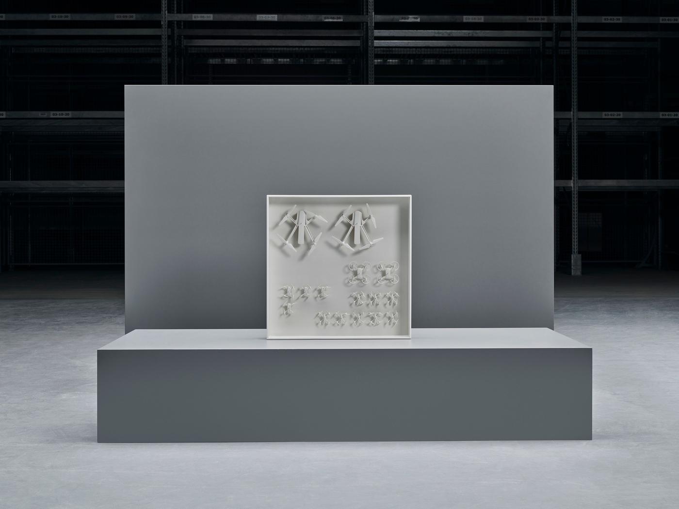 A design object comprising of white drones arranged in a white container on display on a grey plinth.