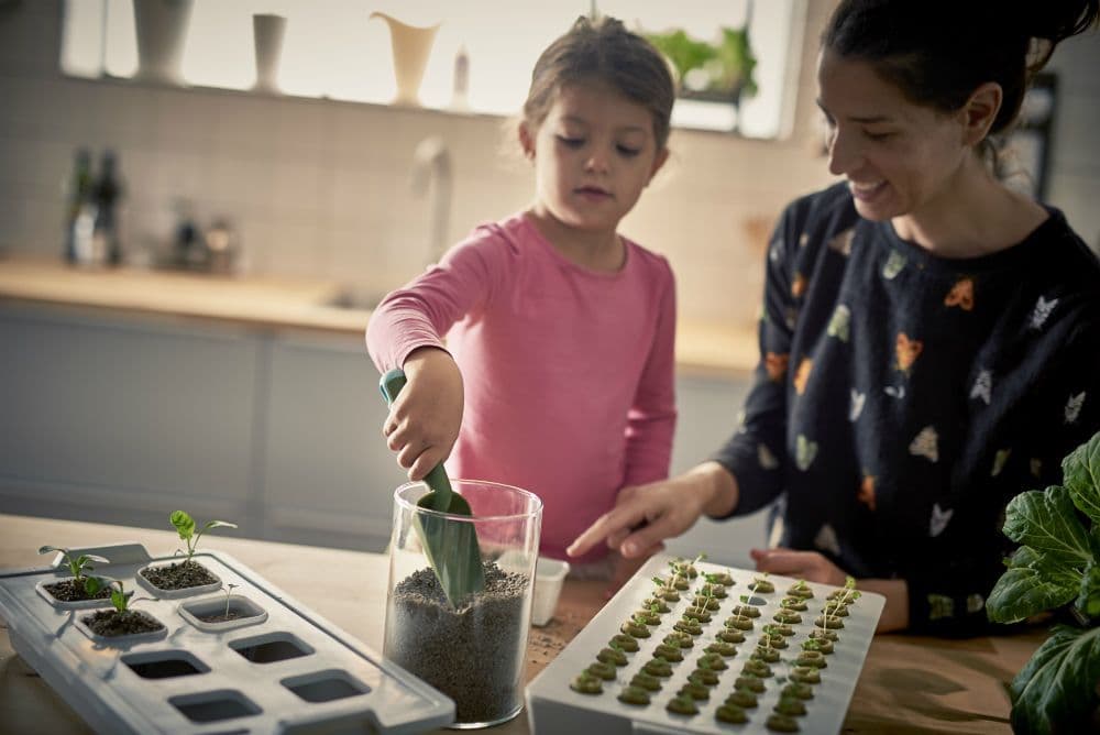 A mother and child potting seedlings together in a kitchen.