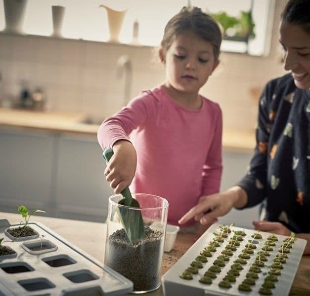Mother and child potting seedlings in a kitchen.