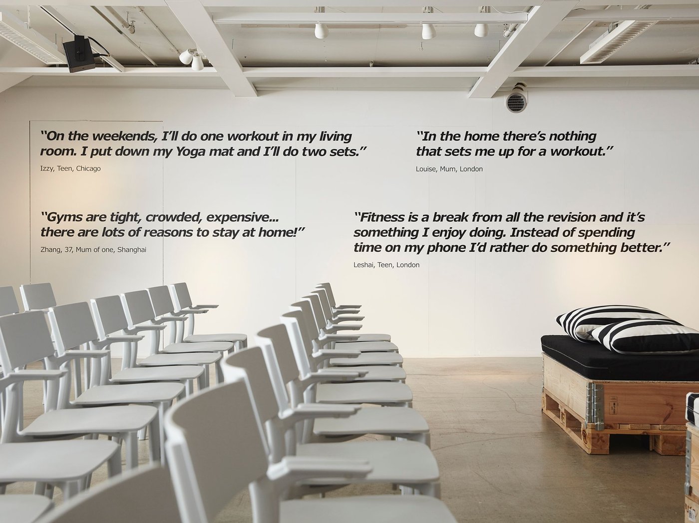 Large white room with rows of empty white chairs.