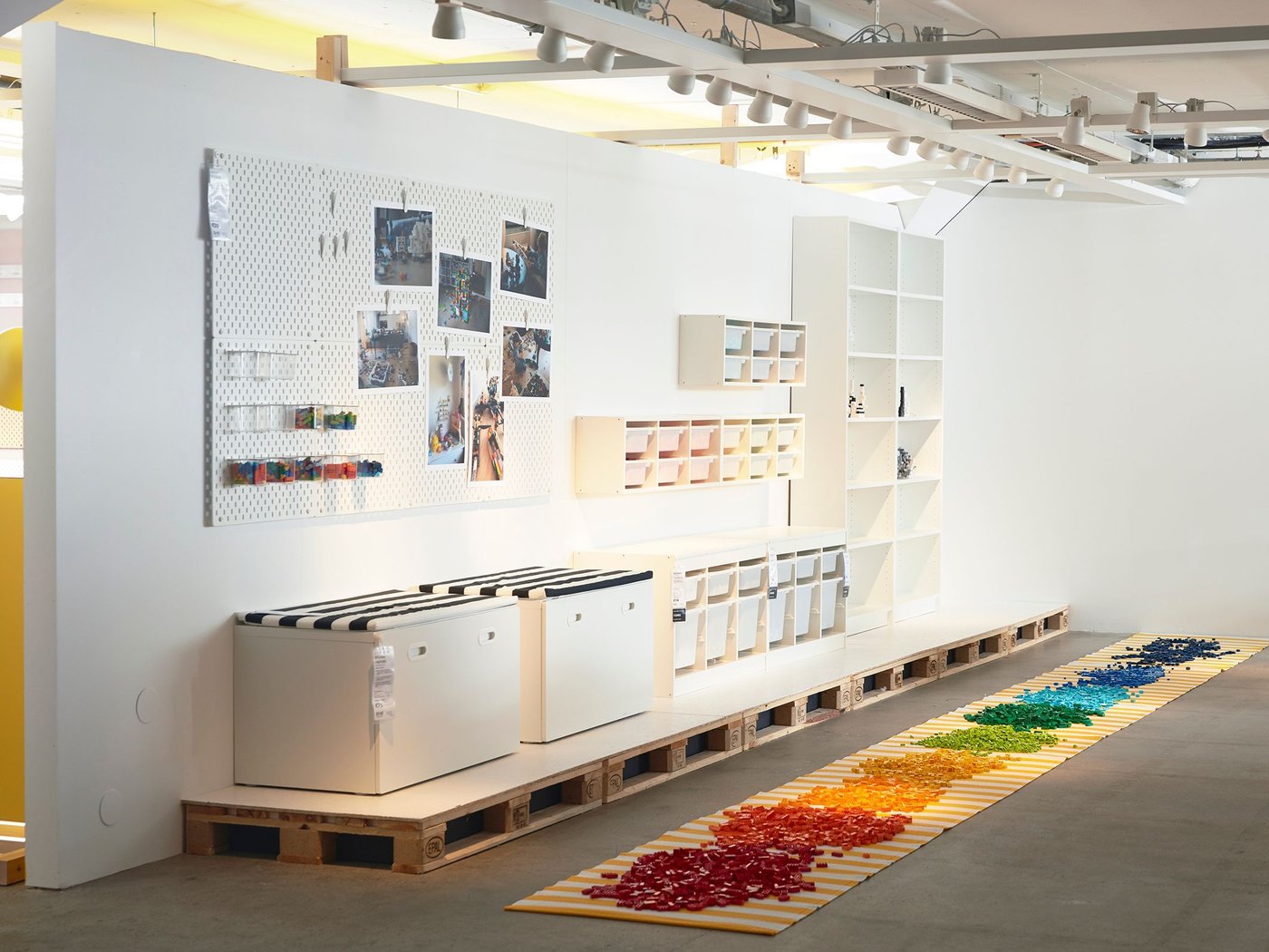 An exhibition space with storage on the walls and lego blocks separated by colour on the floor.