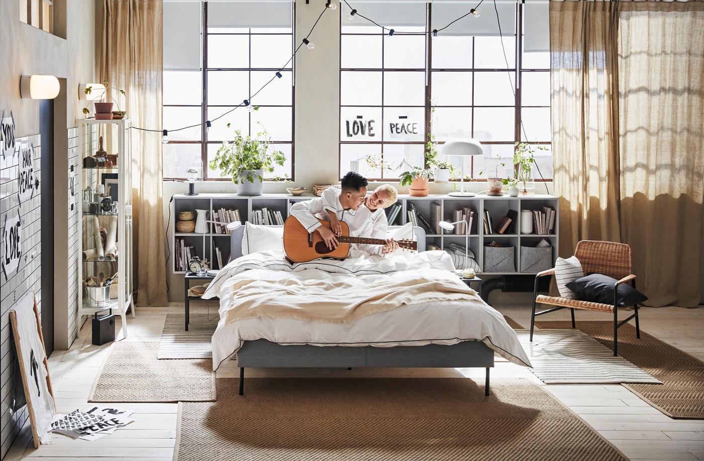 Large bedroom with soft lighting and a couple on the bed playing guitar.