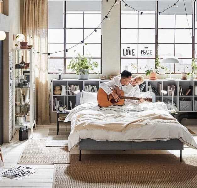 Large bedroom with soft lighting and a couple on the bed playing guitar.