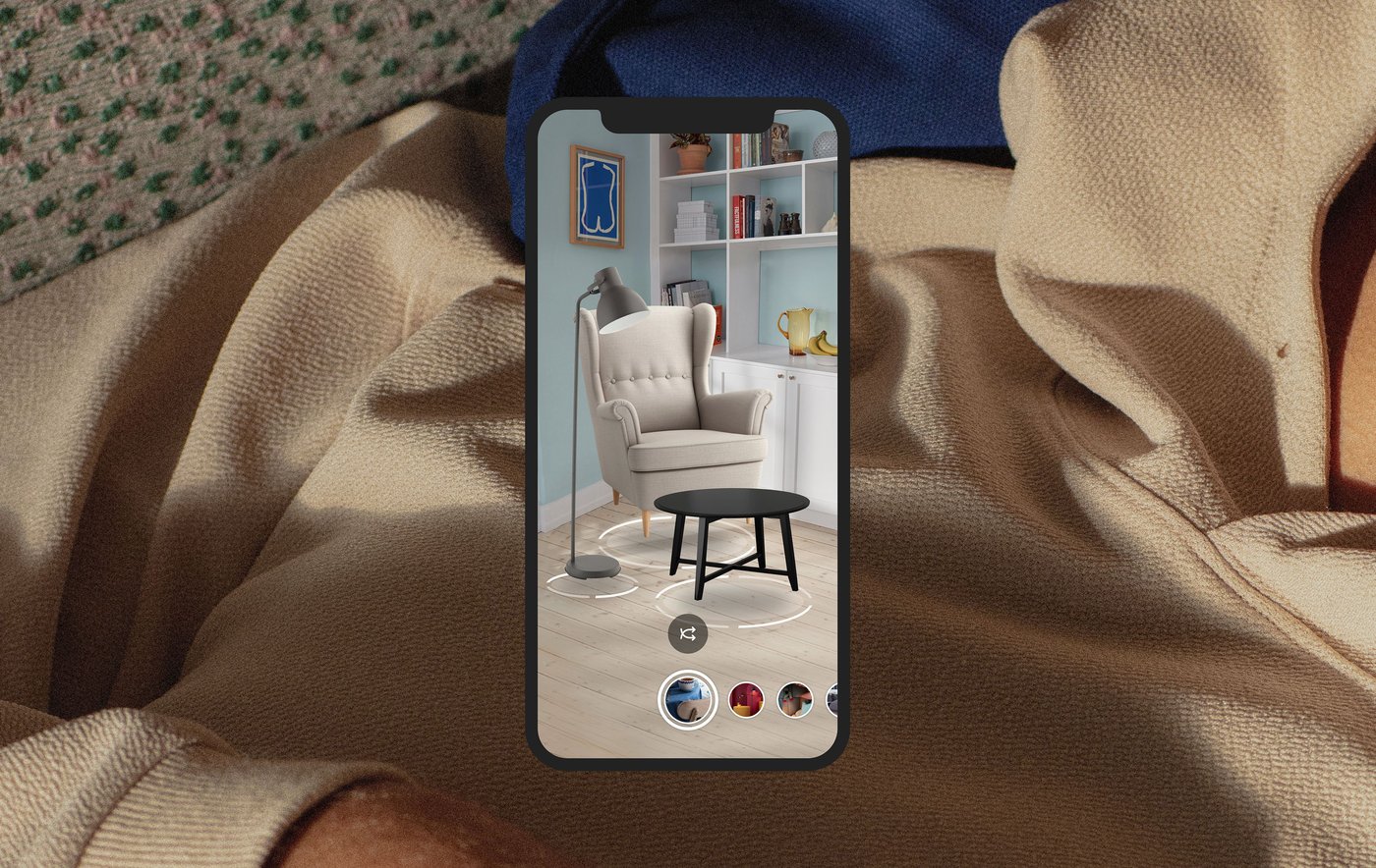 Extreme close up of a person in a beige hoodie, overlaid with a smartphone screen showing a STRANDMON armchair and KRAGSTA coffee table with different colour swatches. 