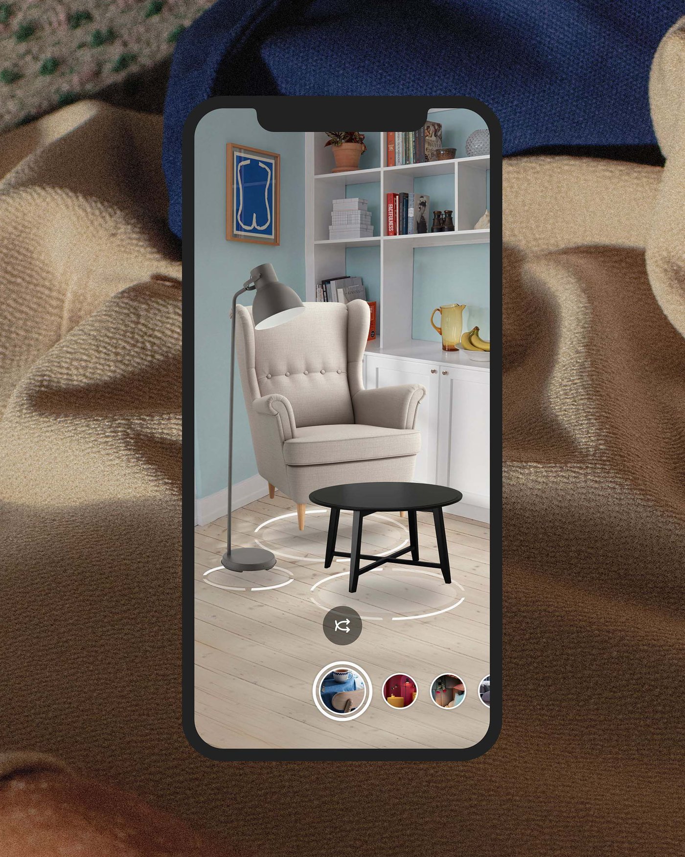 Extreme close up of a person in a beige hoodie, overlaid with a smartphone screen showing a STRANDMON armchair and KRAGSTA coffee table with different colour swatches. 