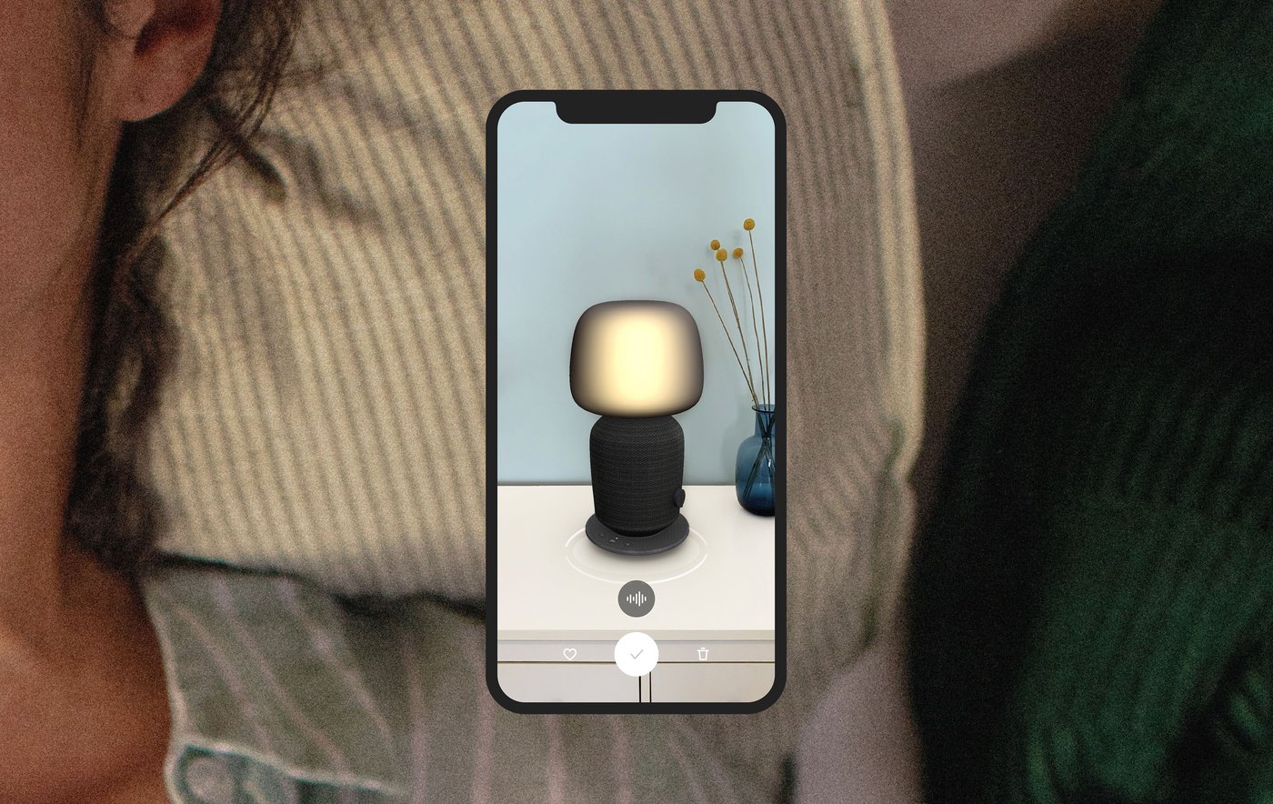 Extreme close up of a pillow with hints of a person's neck and face, overlaid with a smartphone screen showing the SYMFONISK speaker lamp.