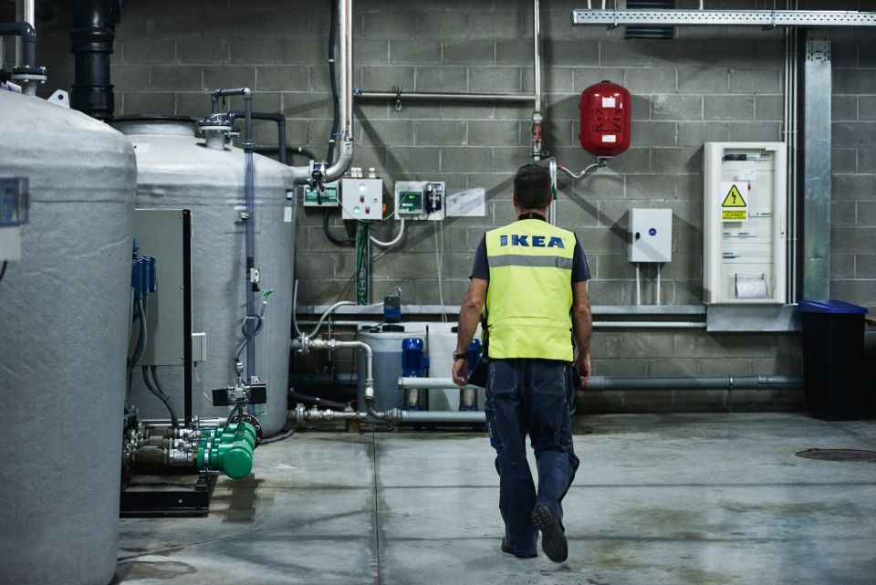 Person in a reflective yellow IKEA safety vest walking through an industrial facility past large tanks.