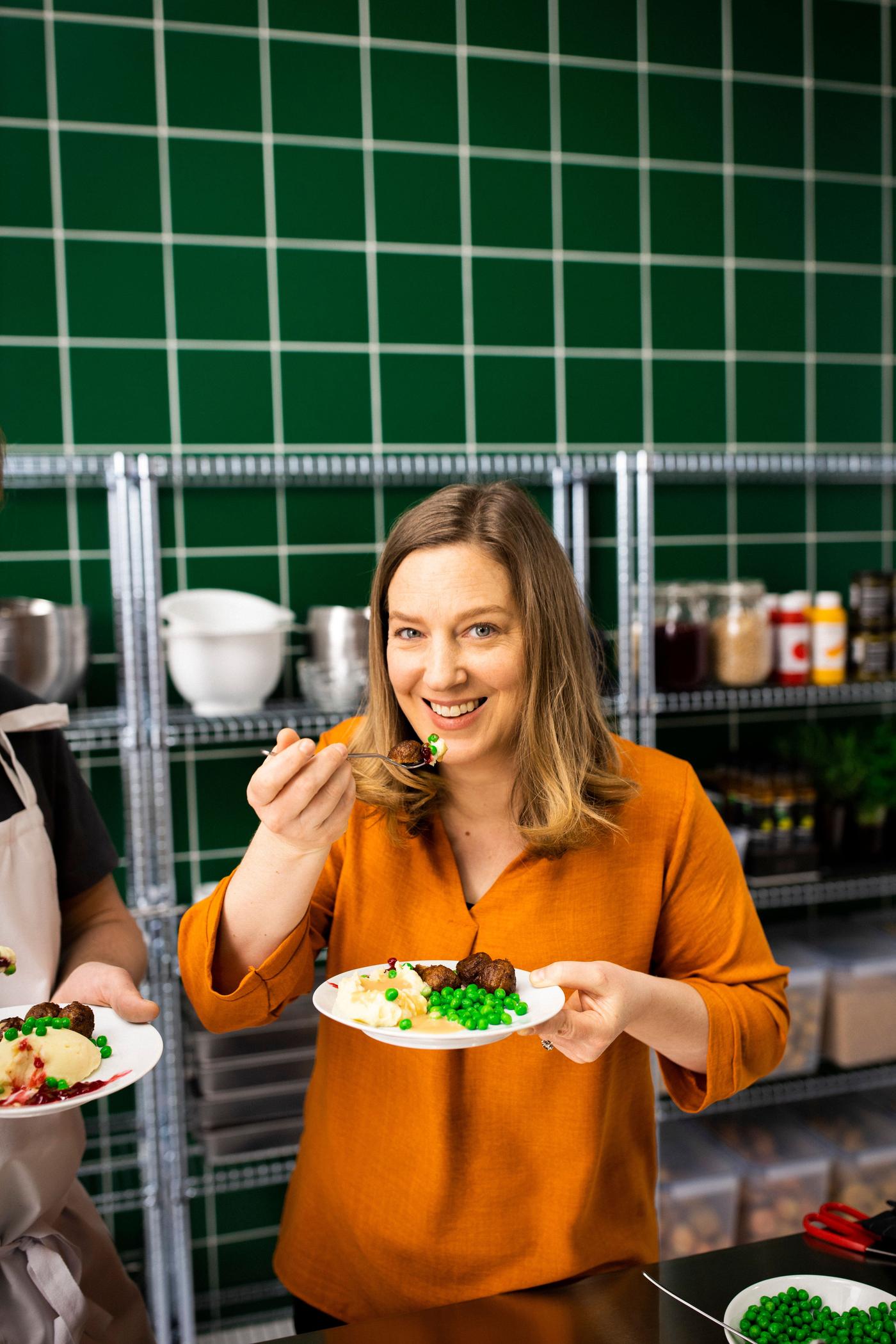 A woman smiles as she tastes a plate of food. 