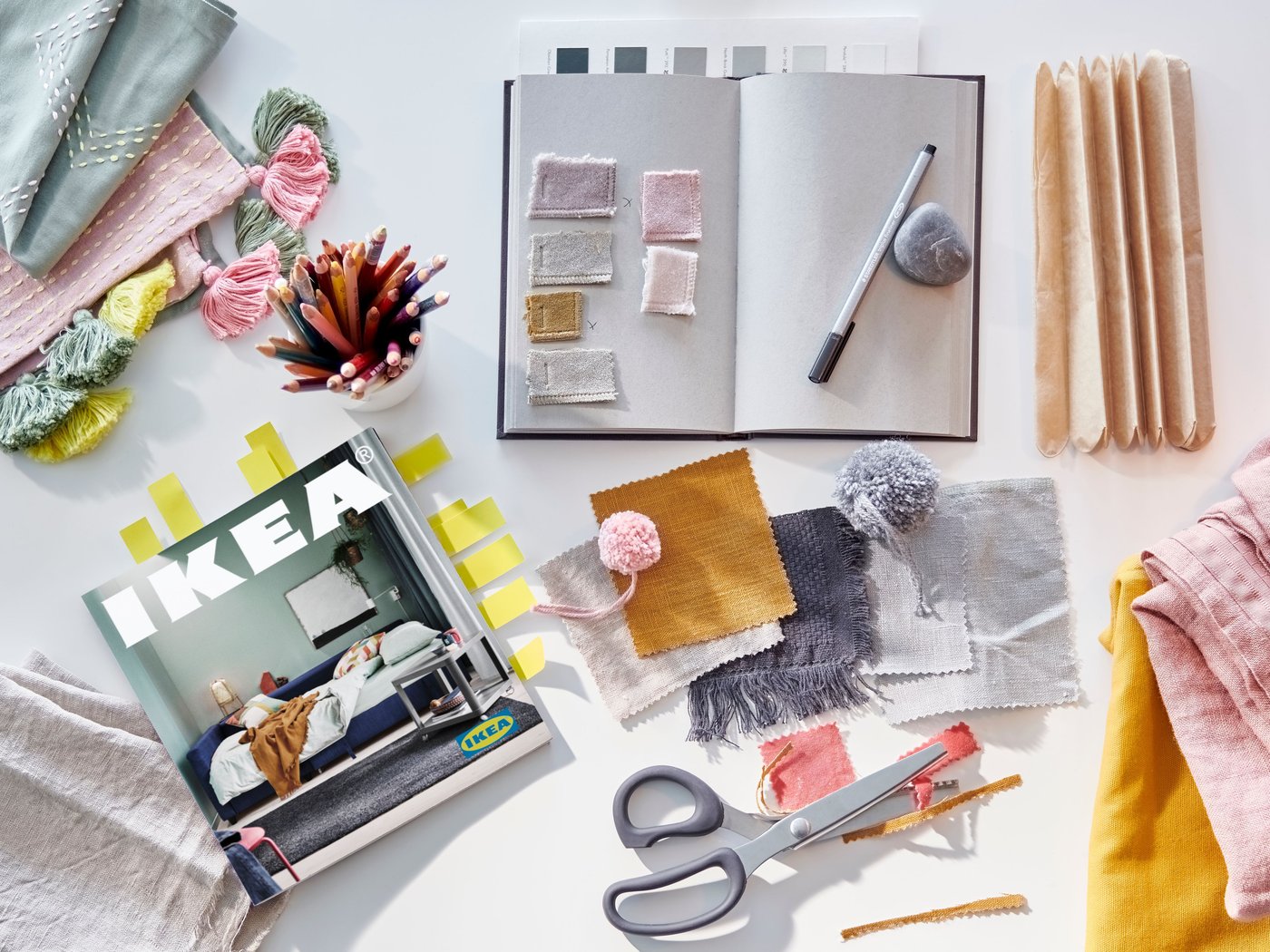 A desk with an IKEA catalogue with sticky notes, a notebook, scissors and fabric swatches.