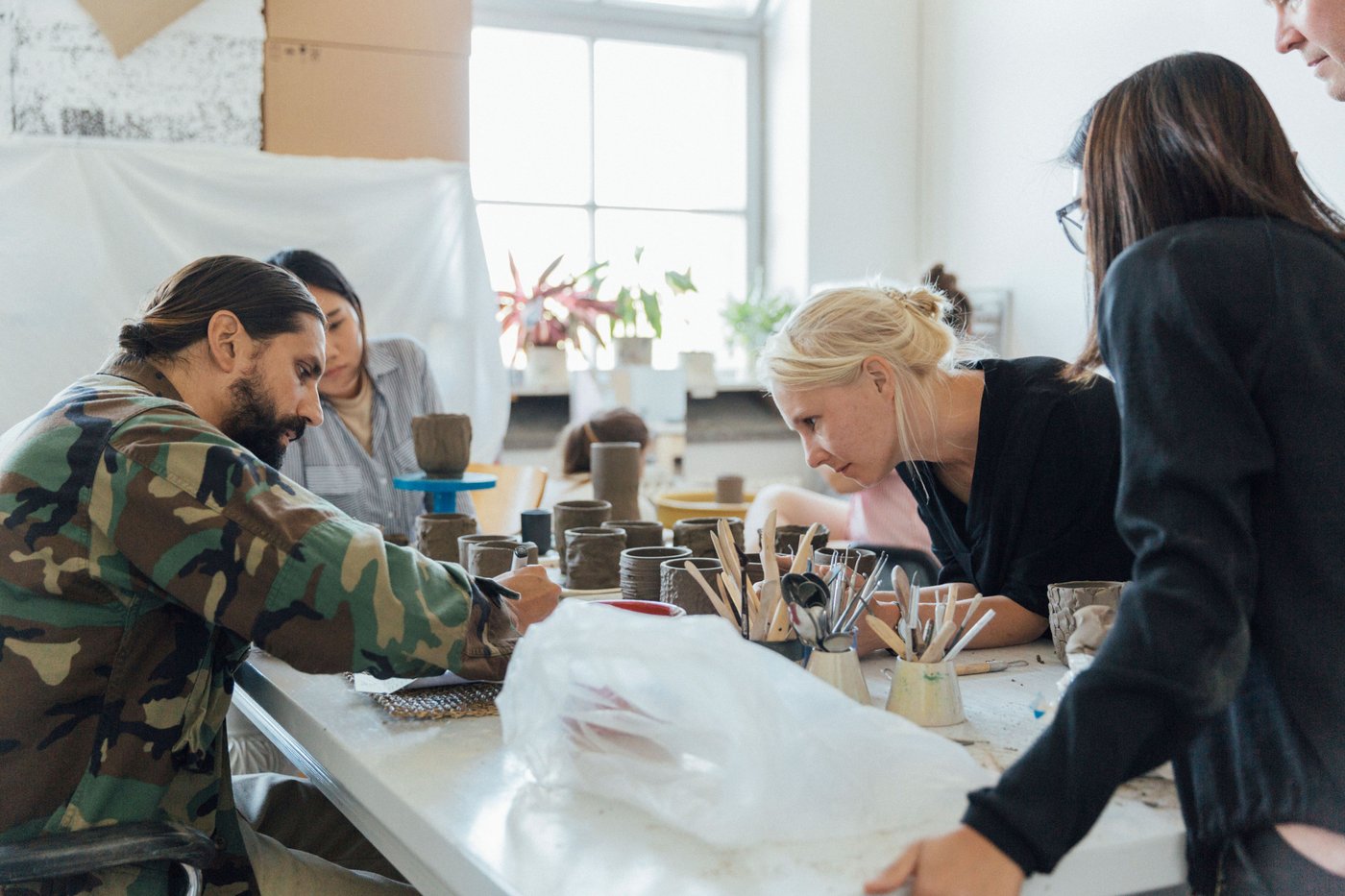 A group of people gather around a table. They are looking at a man forming with clay.
