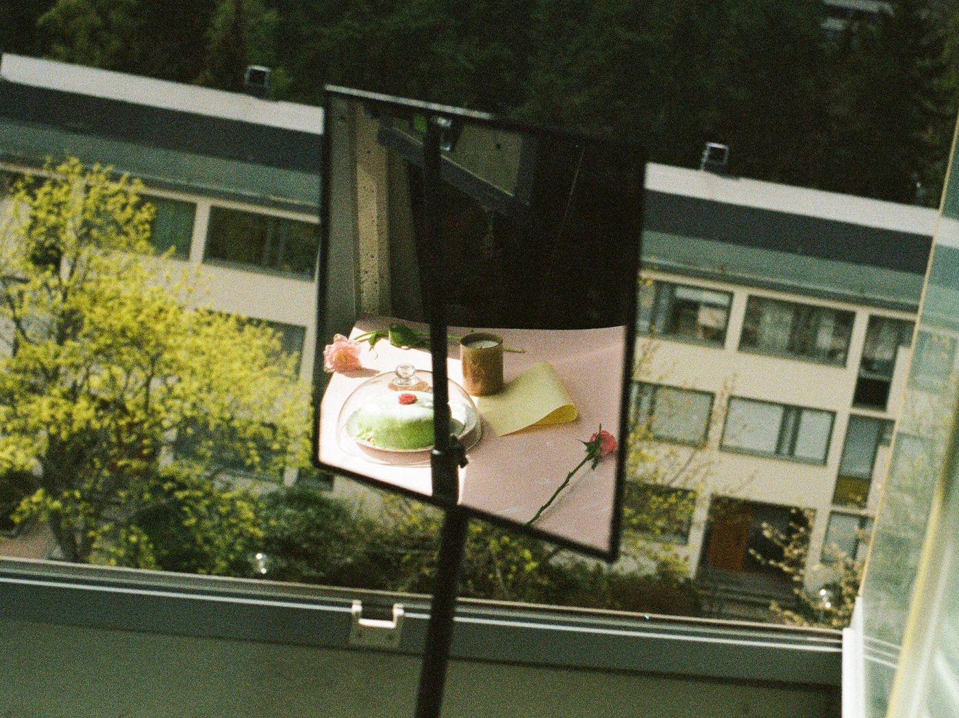 A mirror in front of a window reflects a table with cake and a candle.