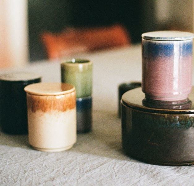 Three ceramic vessels holding candles stand on a wood table. Another sits on top of a ceramic container.