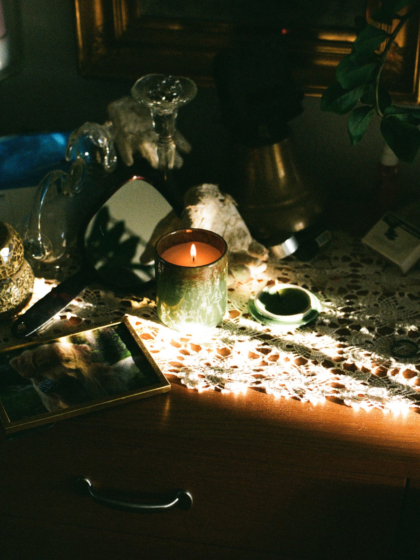 A table with a crochet runner and a ceramic candle burning. The sun shines through, casting shadows.
