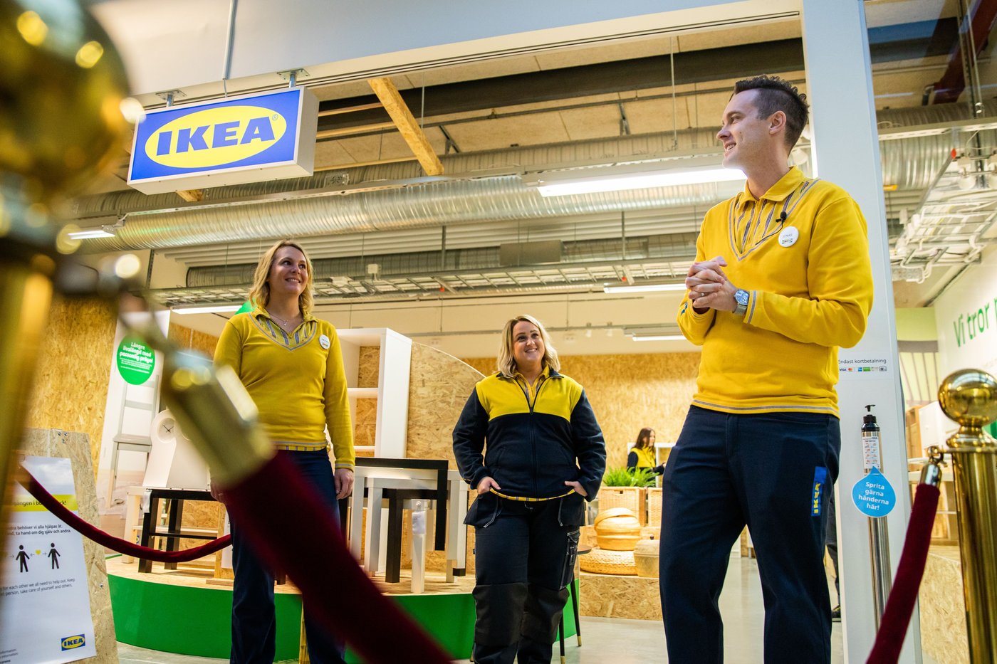 Three IKEA co-workers stand at the front of the IKEA secondhand shop. There is an IKEA sign above. They are all smiling.