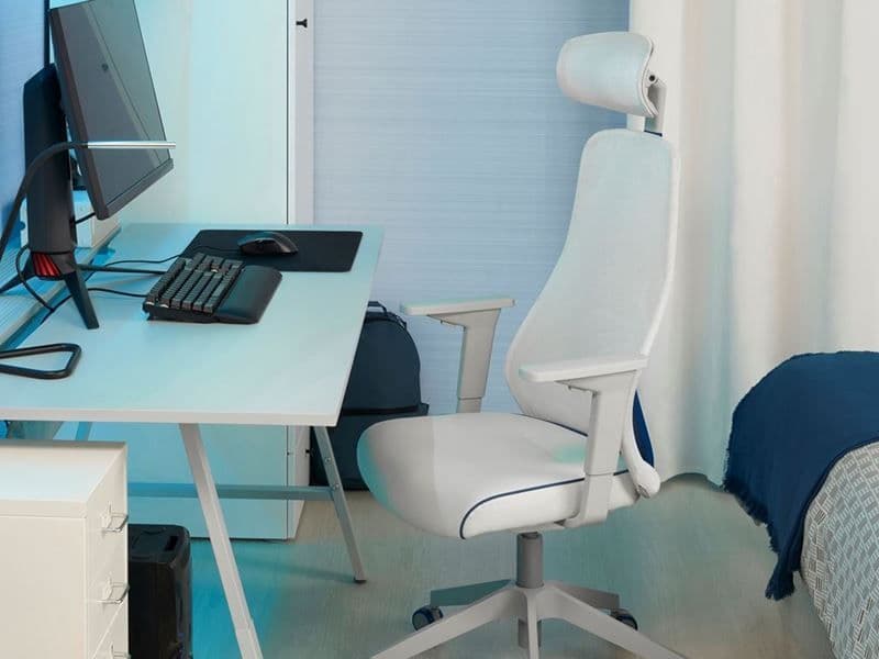 A white gaming chair is placed next to a white desk. The desk has a black monitor and keyboard.