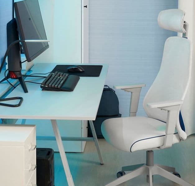 A white gaming chair is placed next to a white desk. The desk has a black monitor and keyboard.