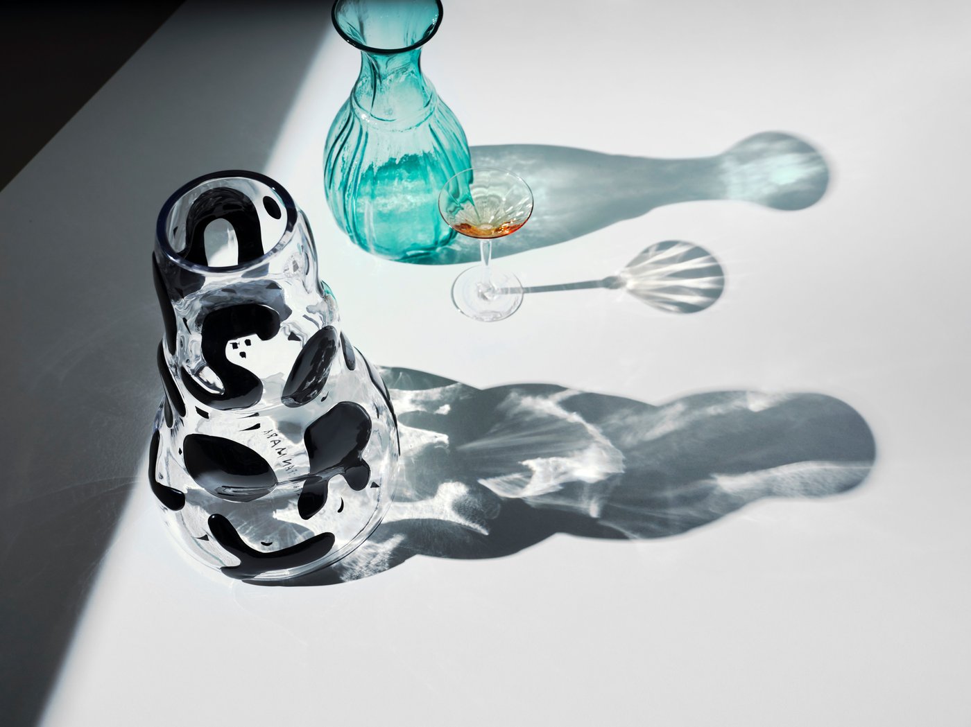 A black and clear vase and a blue vase on a white surface. The light shines through them.