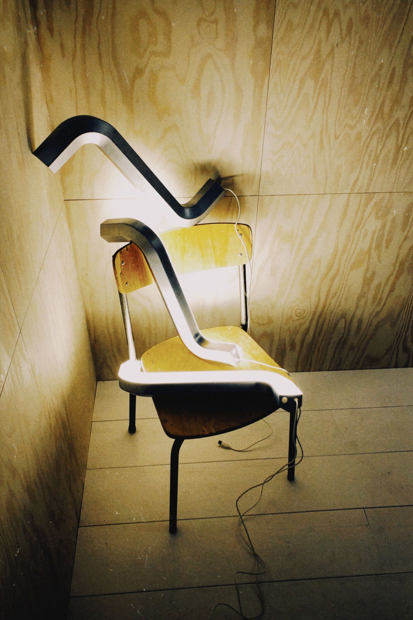 Three illuminated allen key lights sit on a chair and from a wood wall in the corner.