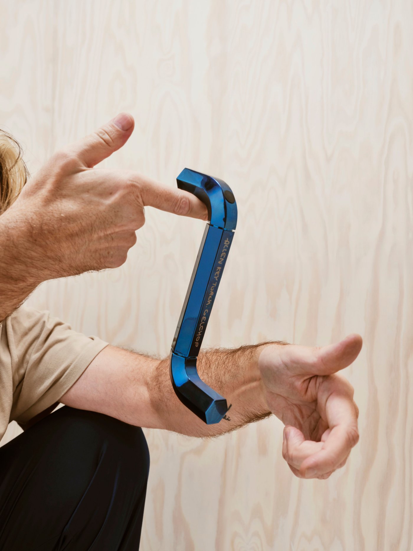 A blue allen key shaped LED torch lamp hangs from a person's finger.