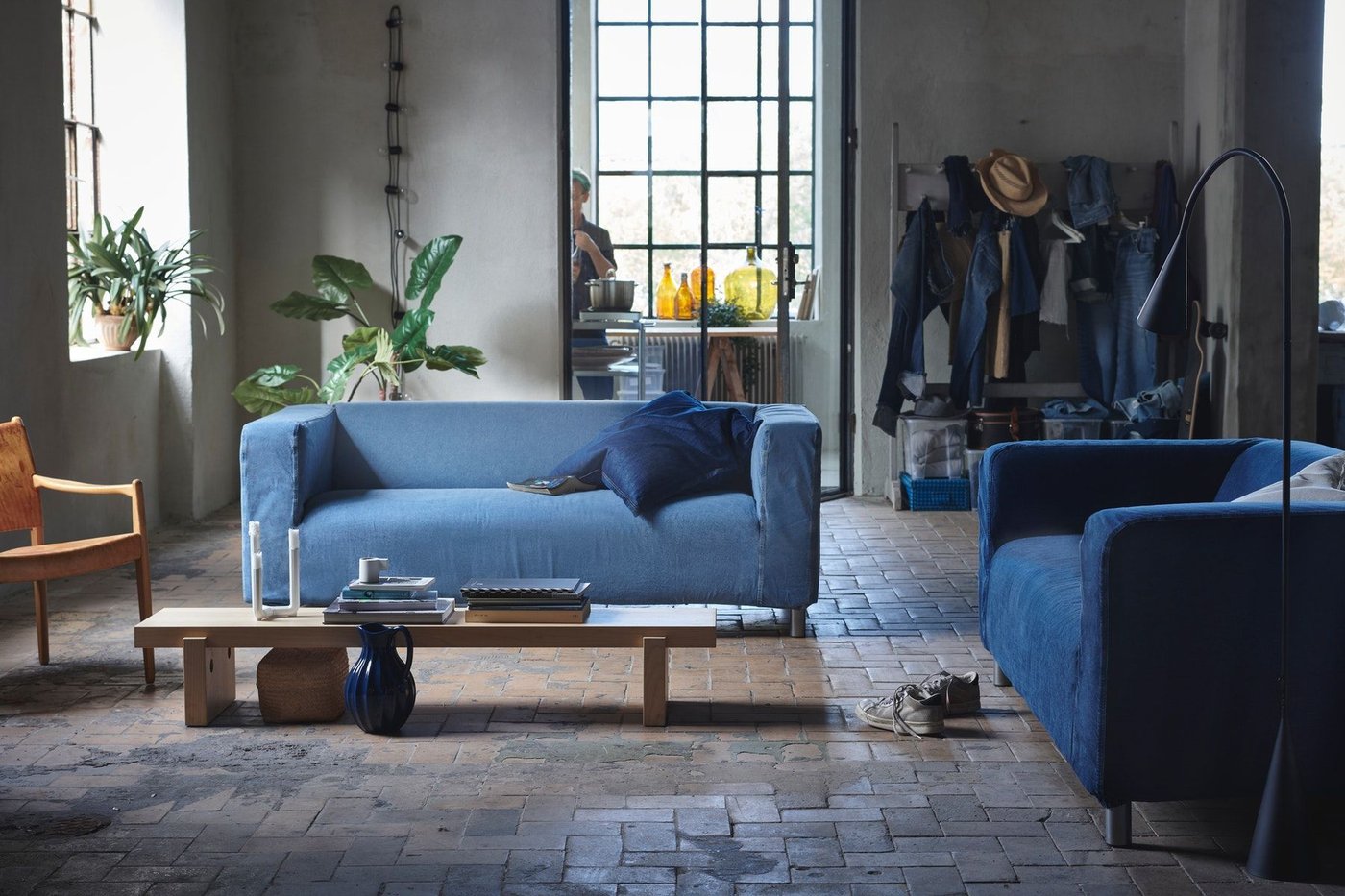 A living room with two denim covered sofas and a long low table in front. In the background are windows and plants.
