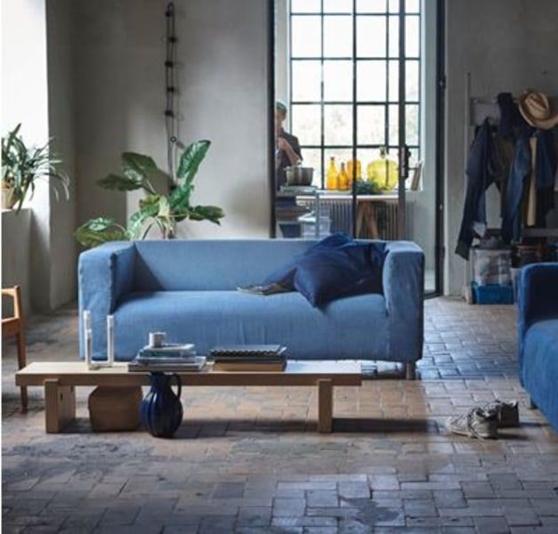 A living room with two denim covered sofas and a long low table in front. In the background are windows and plants.