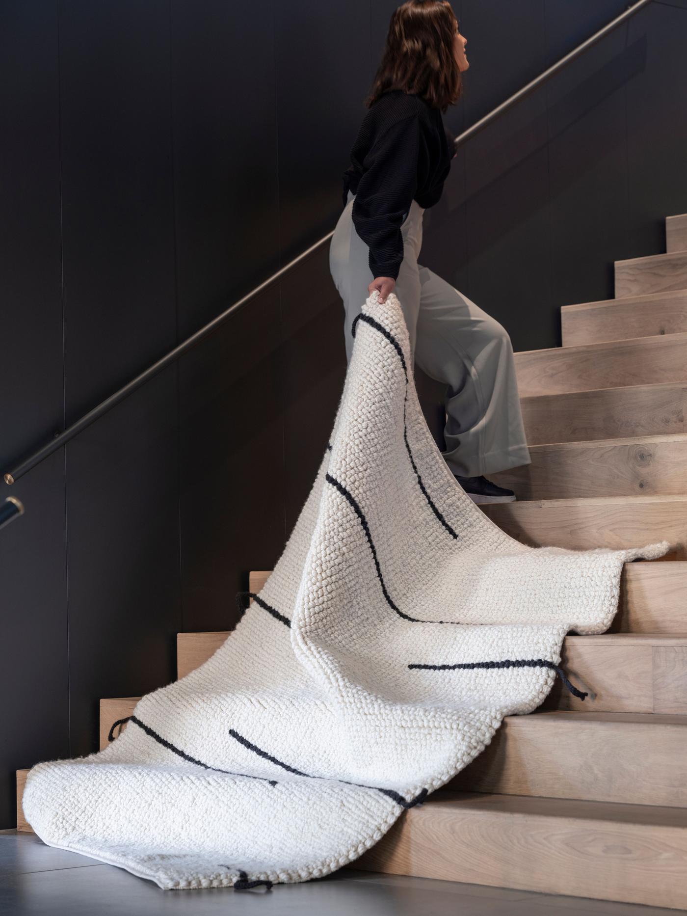A person drags a white rug with black lines up a wide staircase.