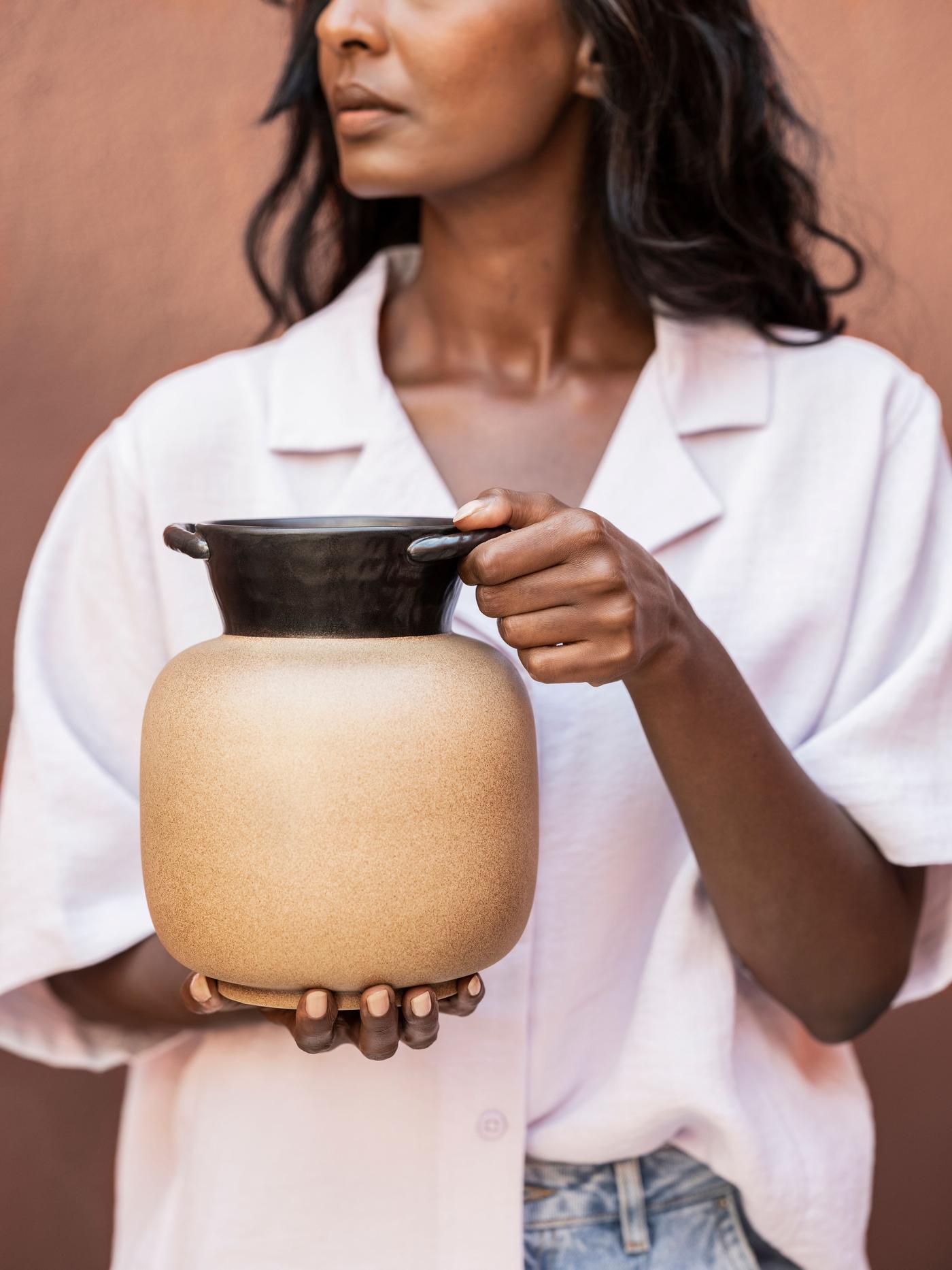 A woman in a white top holds a brown and beige jug in her hands.