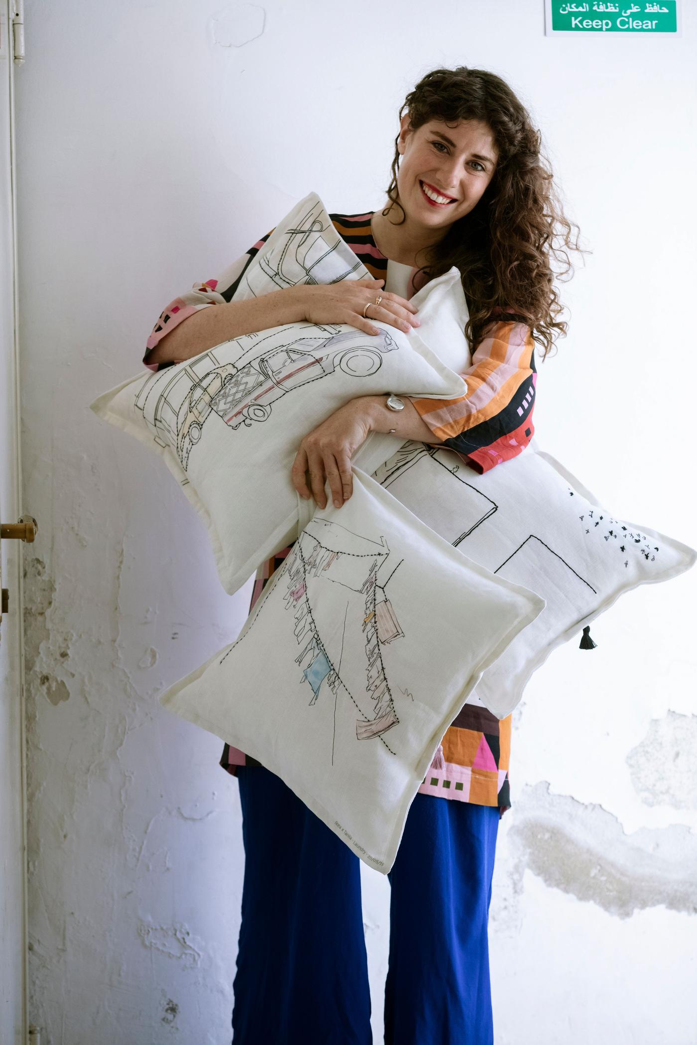 A woman holds three white, printed cushions. She is smiling.