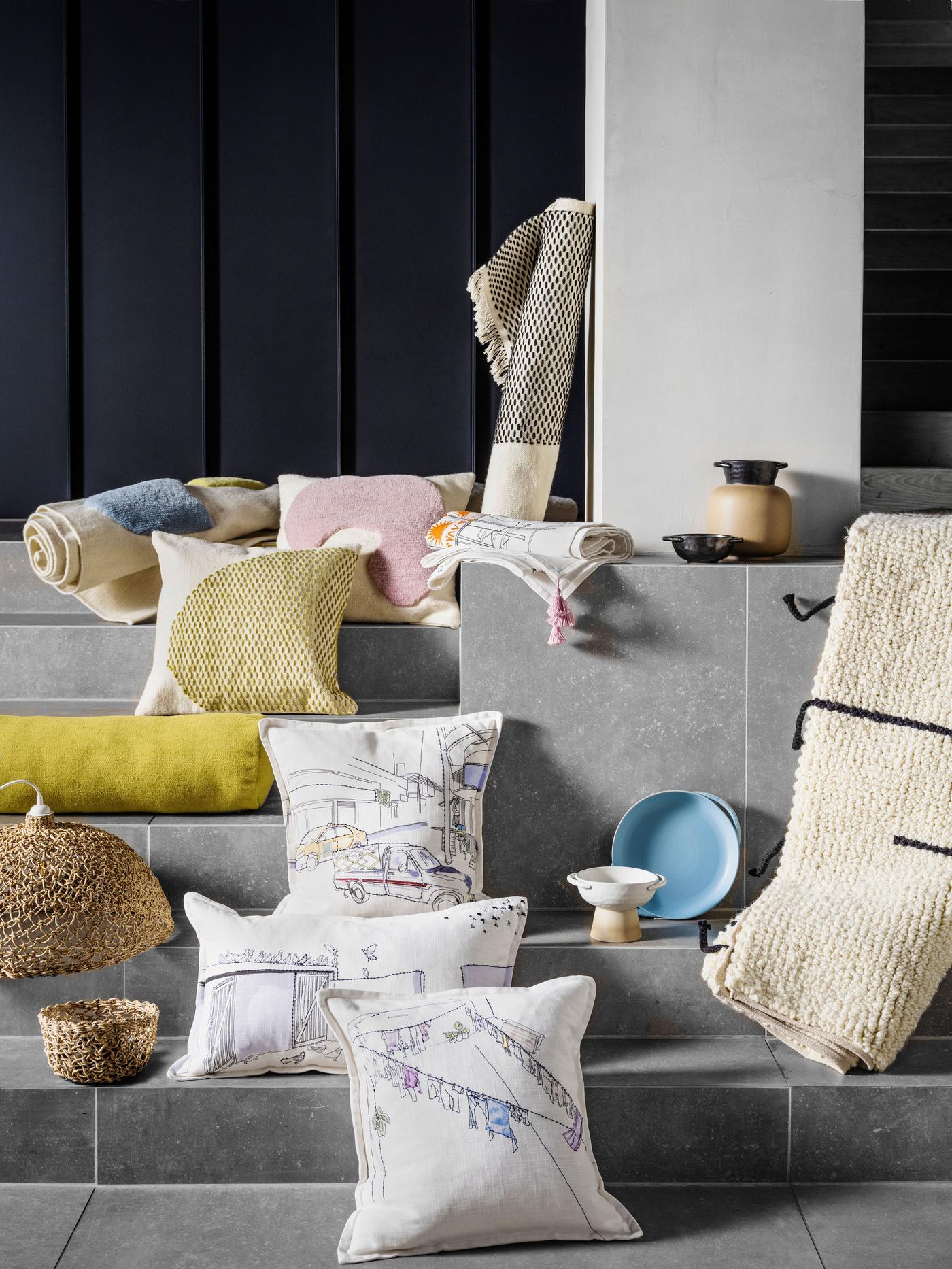 A grey room with steps. There are cushions, rugs and accessories placed on the steps.