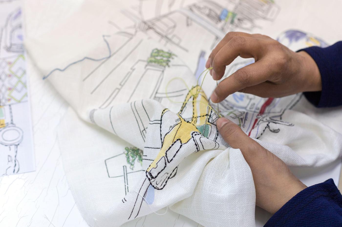 A pair of hands embroider a piece of white printed cloth.